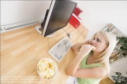 Viennaslide-72000370 Junge Frau isst Chips am Schreibtisch - Young woman eating chips at desk
