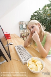 Viennaslide-72000372 Junge Frau isst Chips am Schreibtisch - Young woman eating chips at desk